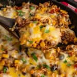 A wooden spoon holding a scoop of taco rice over a skillet.