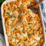 Baked rigatoni and sausage in a blue baking dish with a wooden spoon in it.