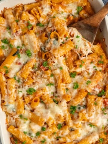 Baked rigatoni and sausage in a blue baking dish with a wooden spoon in it.