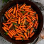Brown sugar honey glazed carrots in a cast iron skillet garnished with fresh parsley.
