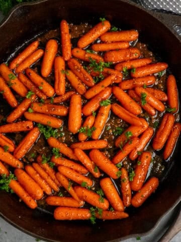 Brown sugar honey glazed carrots in a cast iron skillet garnished with fresh parsley.