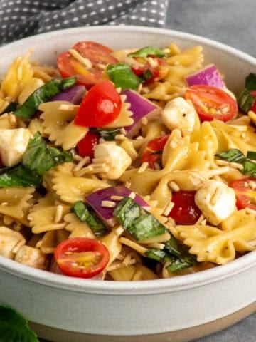 Bruschetta pasta salad in a bowl with a gray dish towel in the background.
