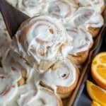 A wooden spatula holding a homemade orange roll with sliced oranges on the side.