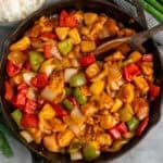 Sweet and sour chicken in a skillet with a wooden spoon.