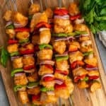Baked chicken skewers stacked on top of each other on a wood cutting board.