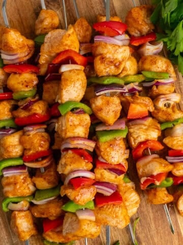 Baked chicken skewers stacked on top of each other on a wood cutting board.