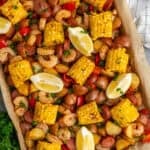 Sheet pan shrimp boil on parchment paper garnished with parsley and lemons.