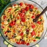 A bowl of spaghetti salad with a wooden spoon resting to the side.