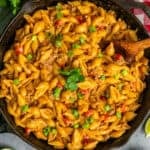 Taco mac and cheese in a cast iron skillet with a wooden spoon.