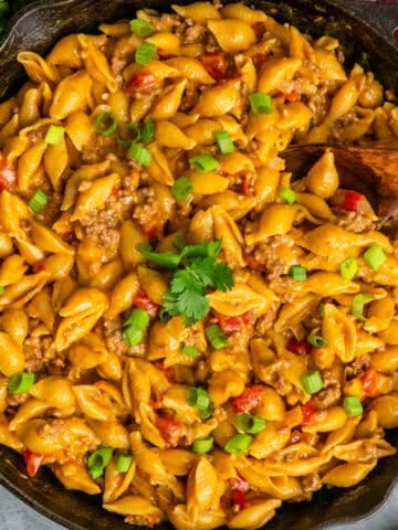 Taco mac and cheese in a cast iron skillet with a wooden spoon.