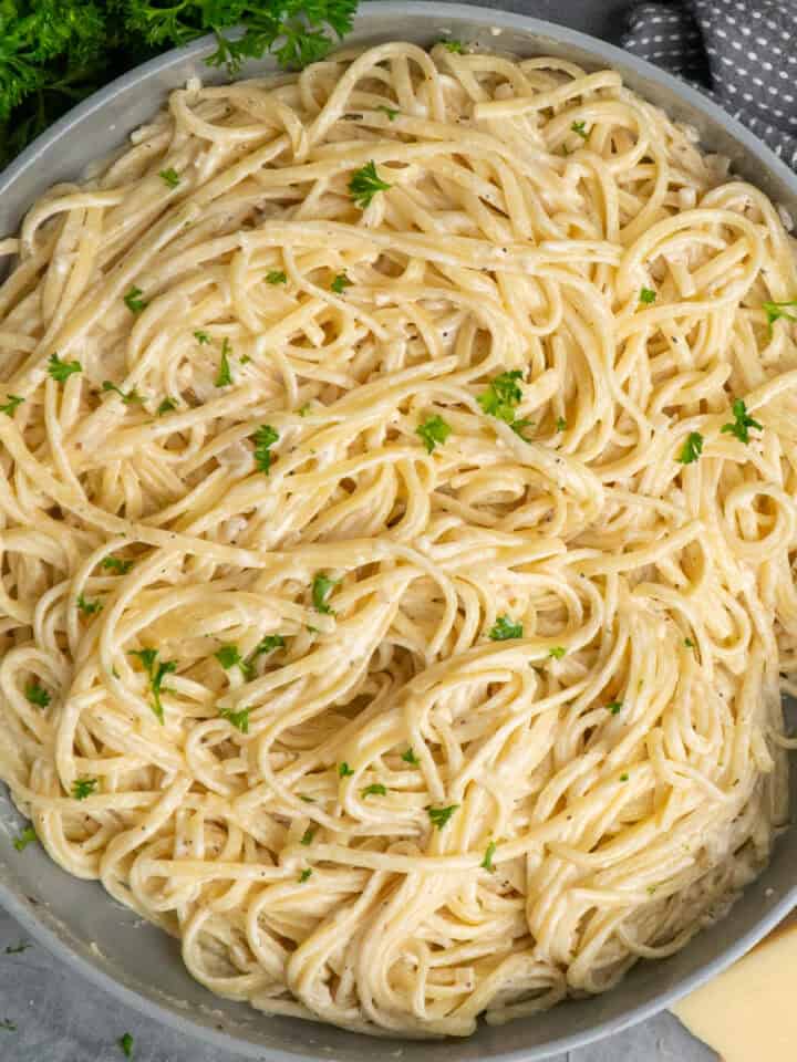 A bowl of garlic butter pasta sprinkled with parsley and parmesan cheese.