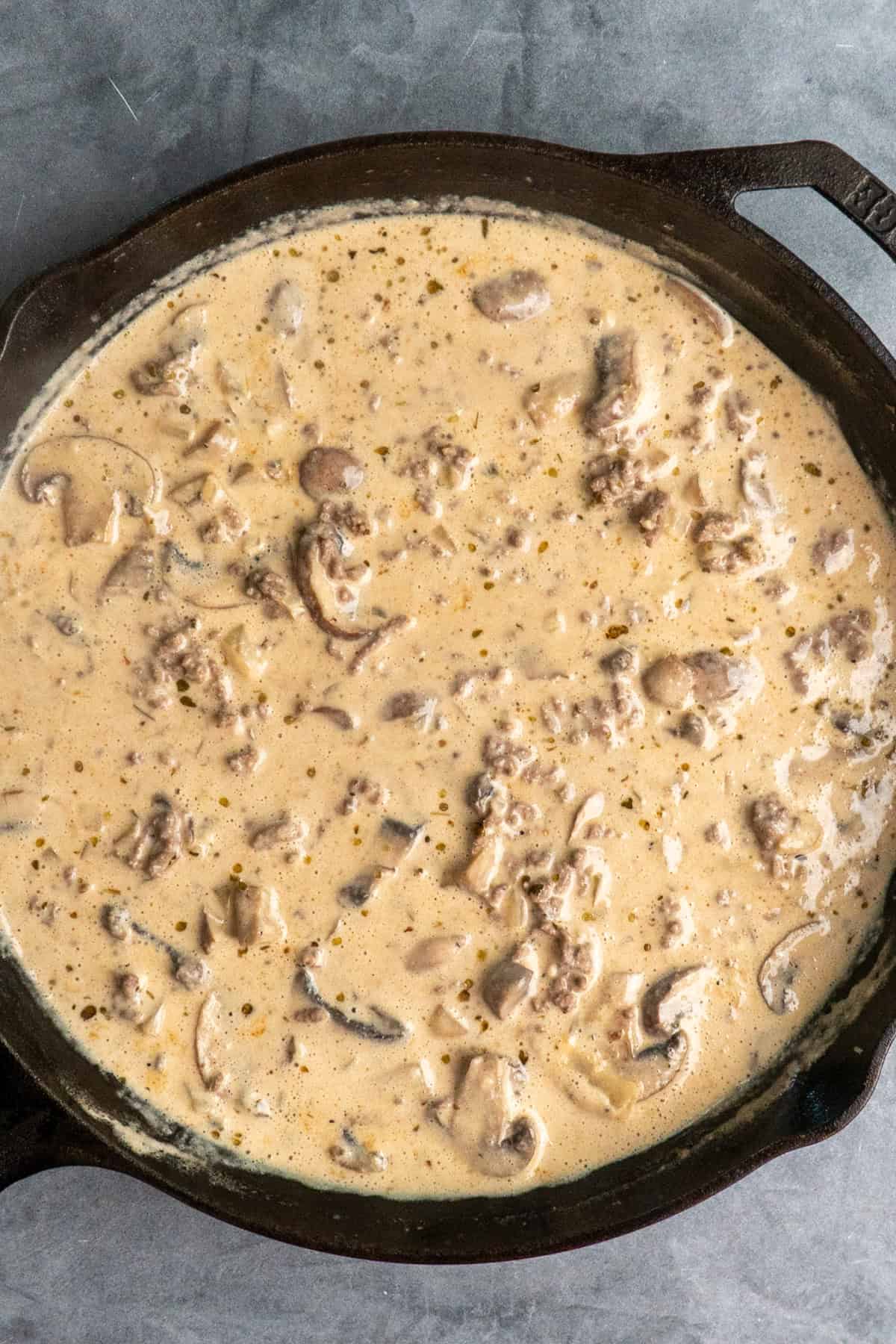 Sauce ingredients mixed together with meat and mushrooms in a skillet.