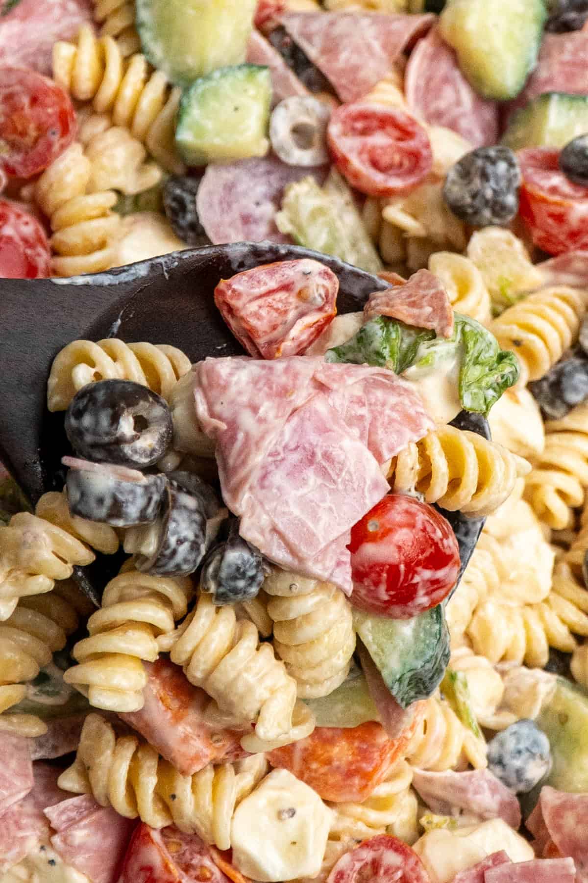 A wooden spoon holding a scoop of Italian grinder pasta salad.