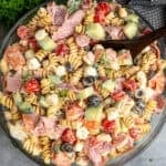 Italian grinder pasta salad in a clear bowl with a wooden spoon in it.