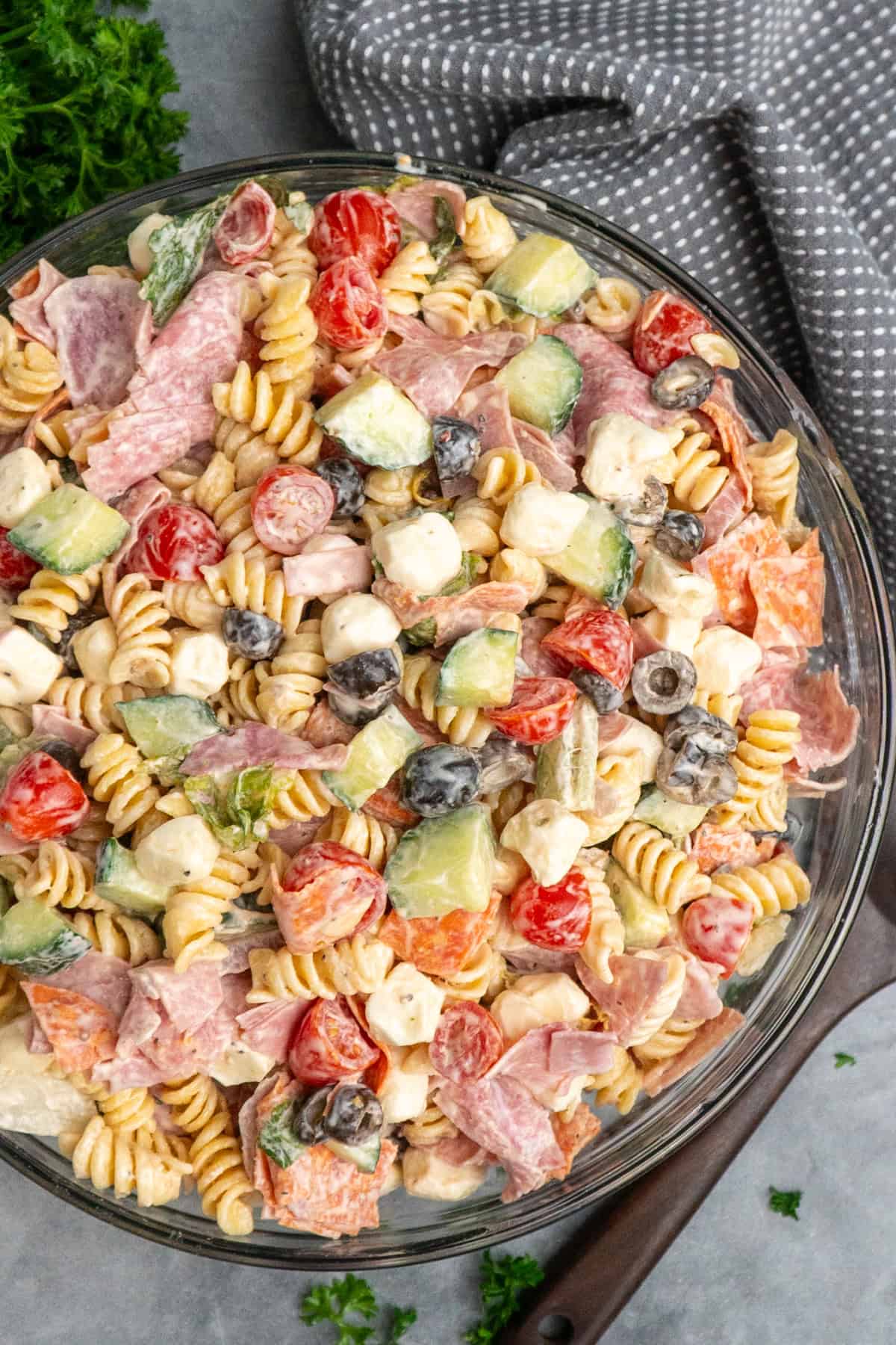 Italian grinder pasta salad in a clear bowl with a wooden spoon in it.