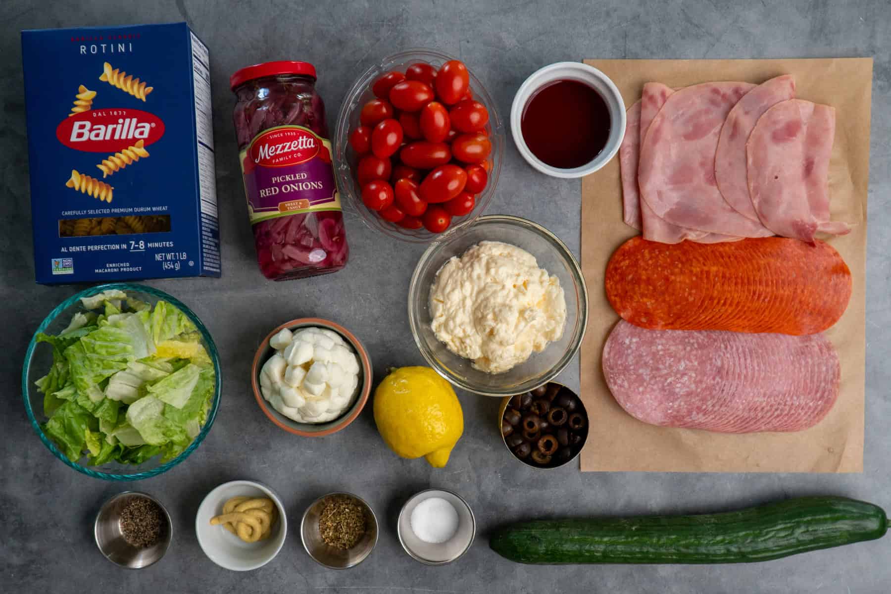 Ingredients for Italian grinder pasta salad on a gray countertop.