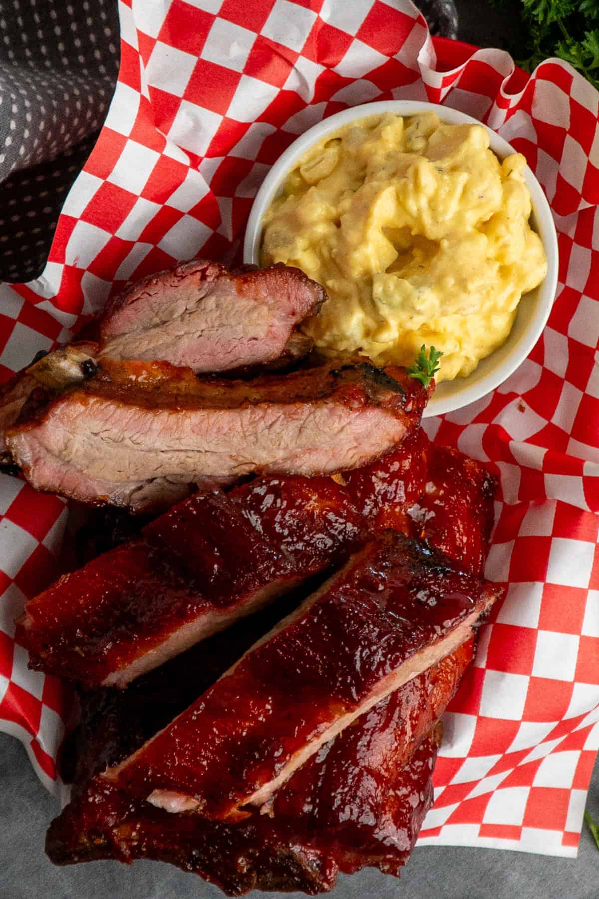 Smoked baby back ribs in a food basket with a side of potato salad.