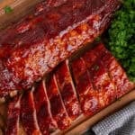 Two racks of smoked baby back ribs on a wood cutting board.