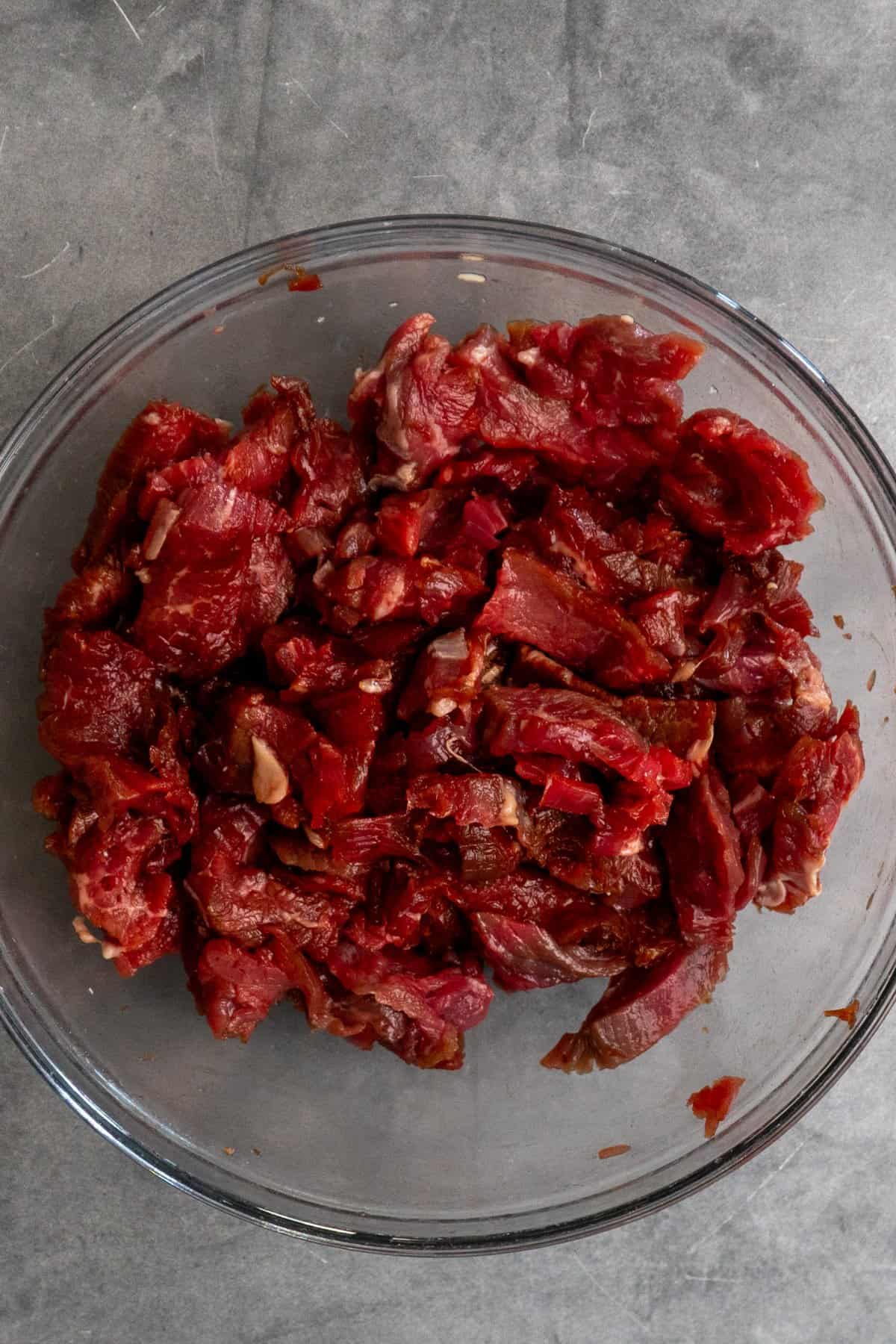 Sliced flank steak marinating in a clear bowl.