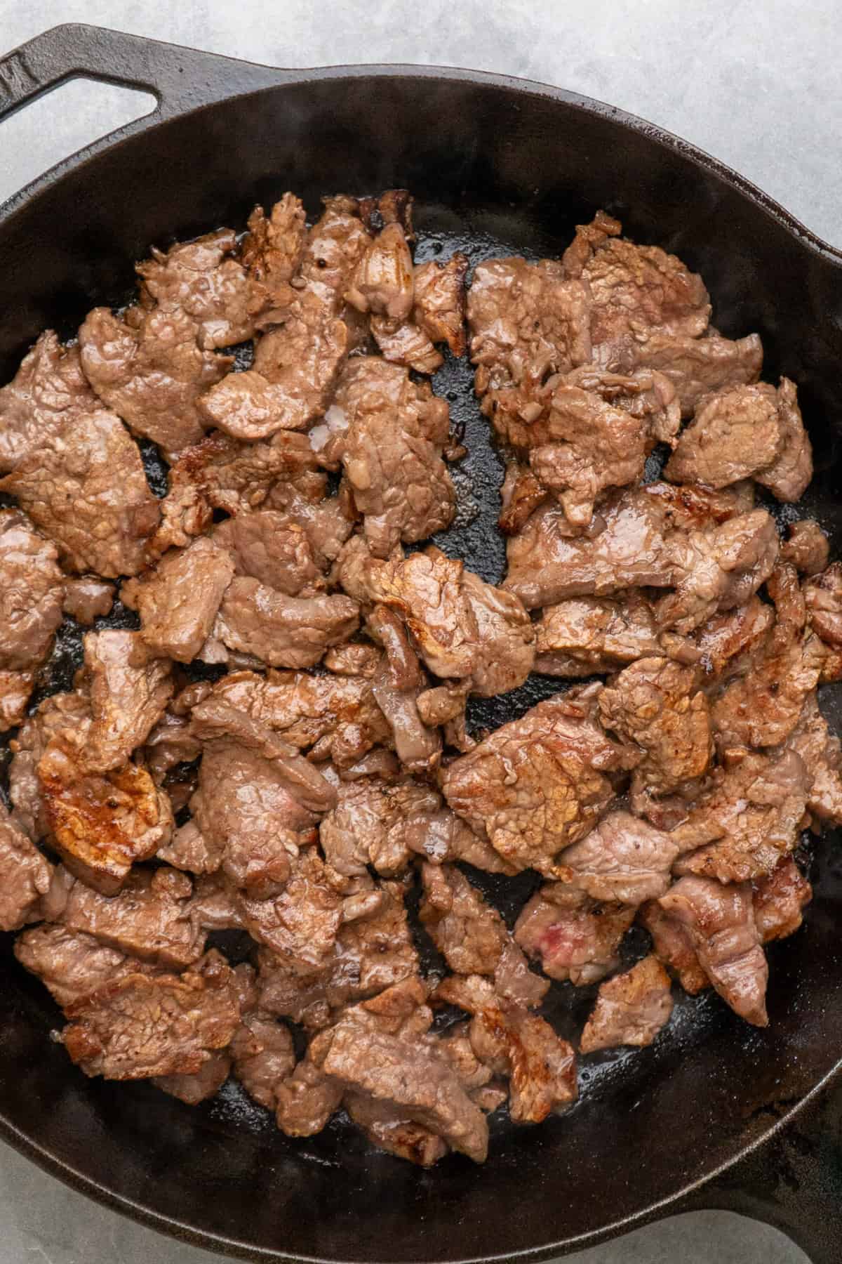 Sliced and marinated steak cooking in a cast iron skillet.