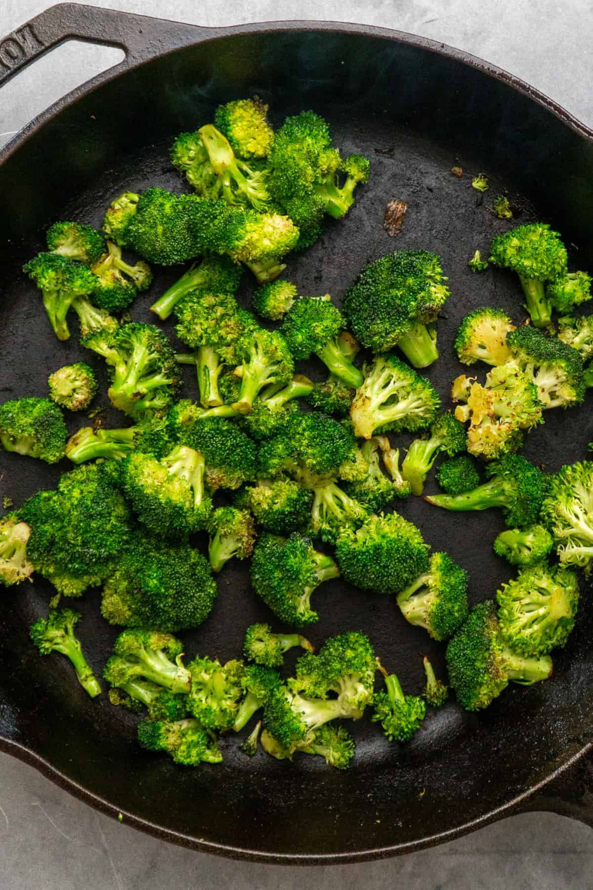 Broccoli florets cooking in a cast iron skillet.