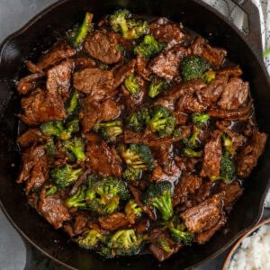 Beef and broccoli in a cast iron skillet with a bowl of rice.