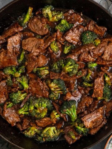 Beef and broccoli in a cast iron skillet with a bowl of rice.