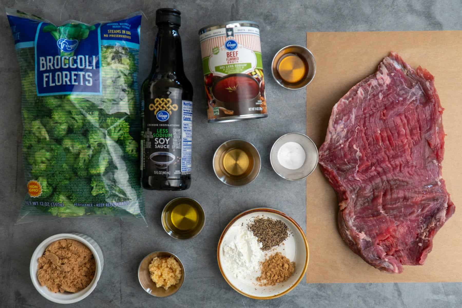 All the ingredients to make beef and broccoli on a gray countertop.