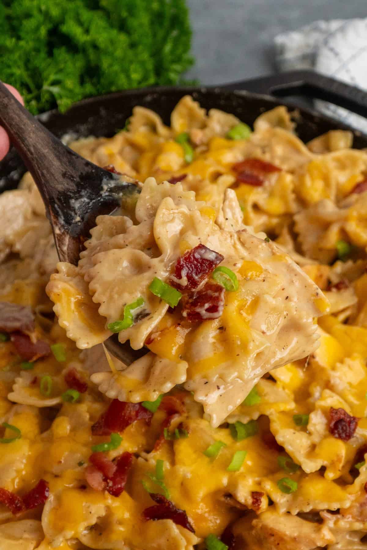 A wooden spoon with a scoop of crack chicken pasta over a skillet.