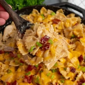 A wooden spoon with a scoop of crack chicken pasta over a skillet.