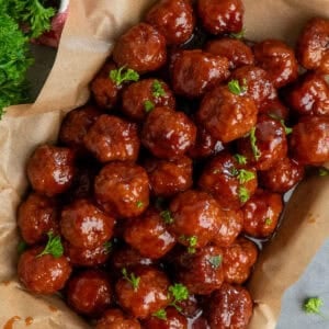 Grape jelly meatballs on a tray covered in parchment paper.