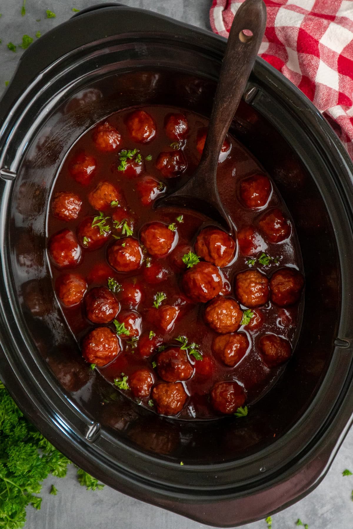 Cooked grape jelly meatballs with a wooden spoon in a crock pot.