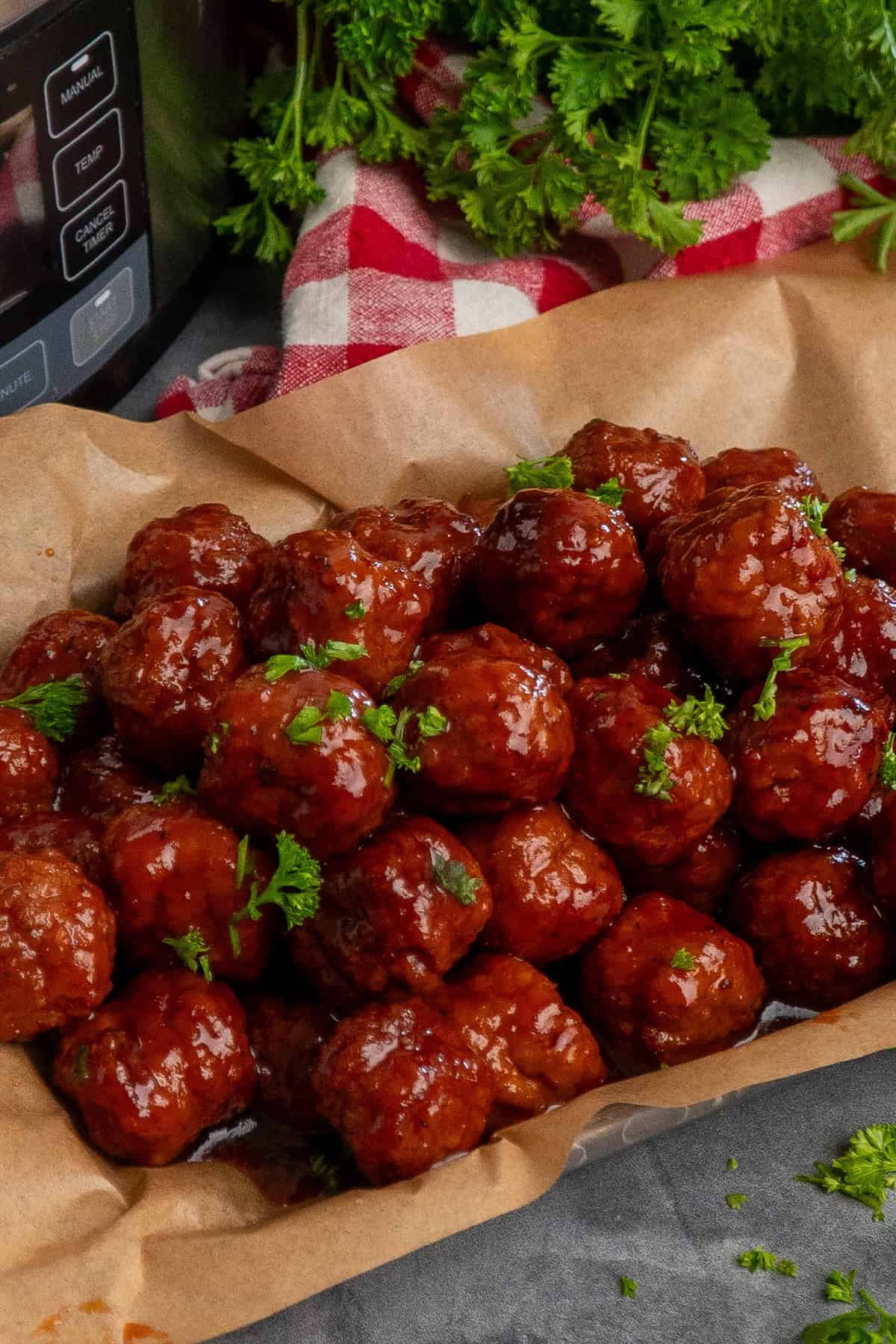 Grape jelly meatballs on a tray covered in parchment paper and parsley in the background.