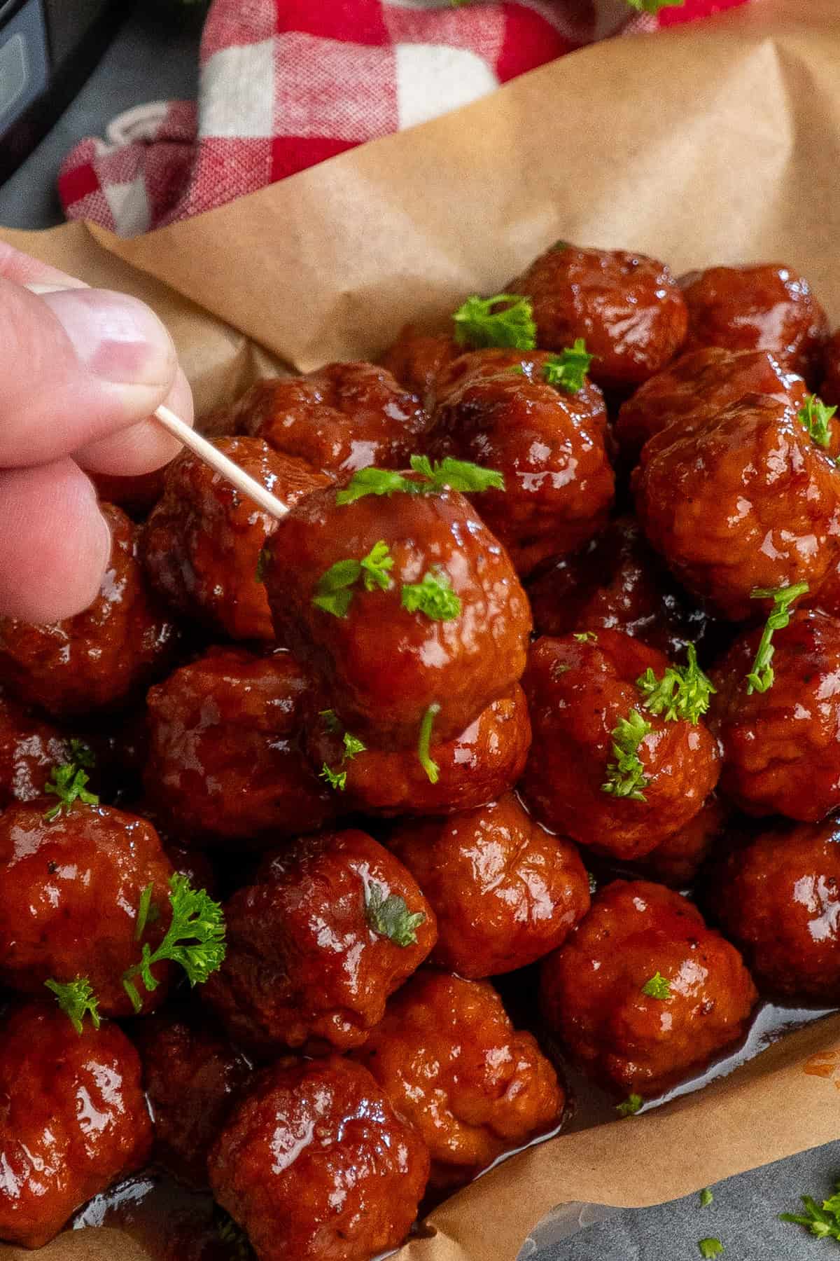 A hand holding a grape jelly meatball on toothpick.