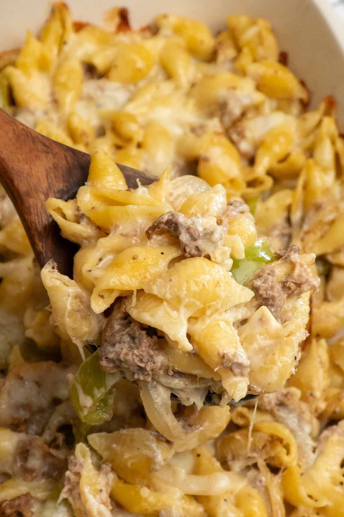 A wooden spoon holding a scoop of Philly cheesesteak casserole.