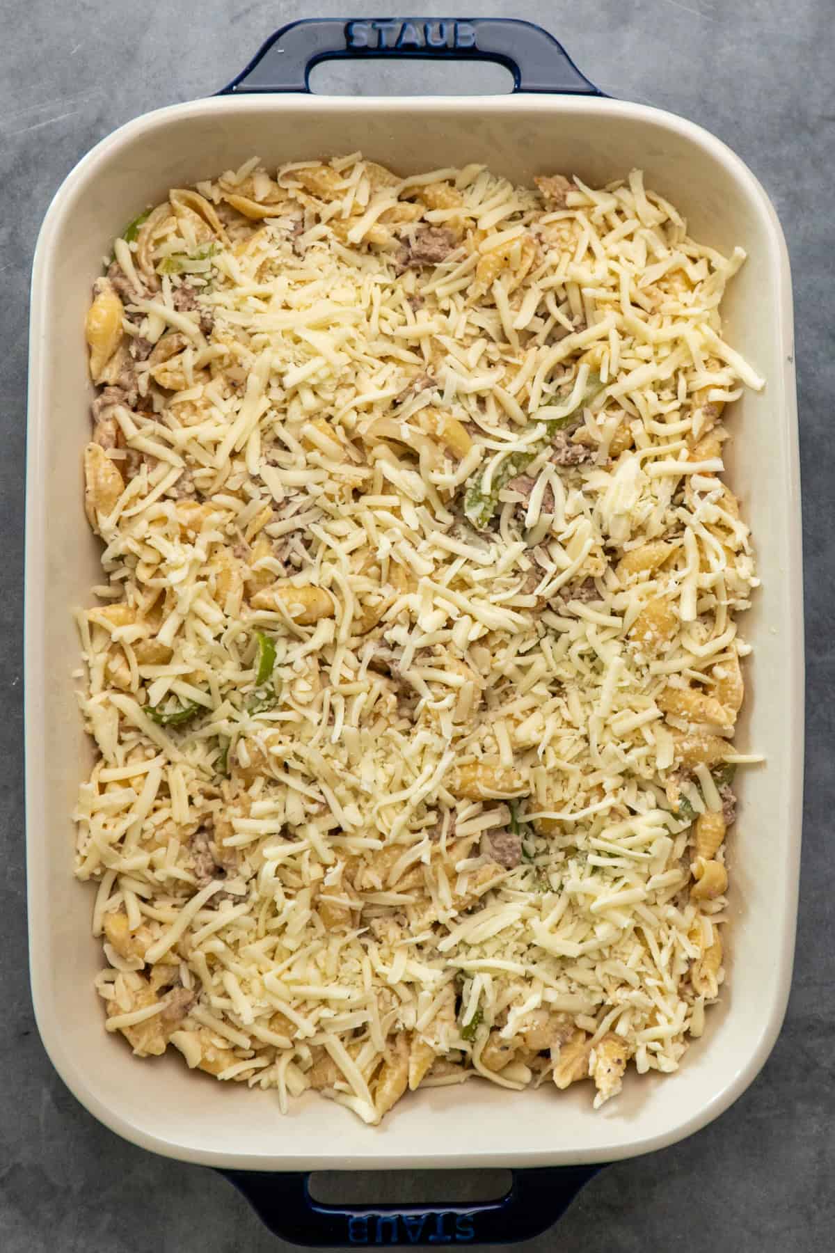 Philly cheesesteak casserole ingredients in a baking dish and topped with cheese.