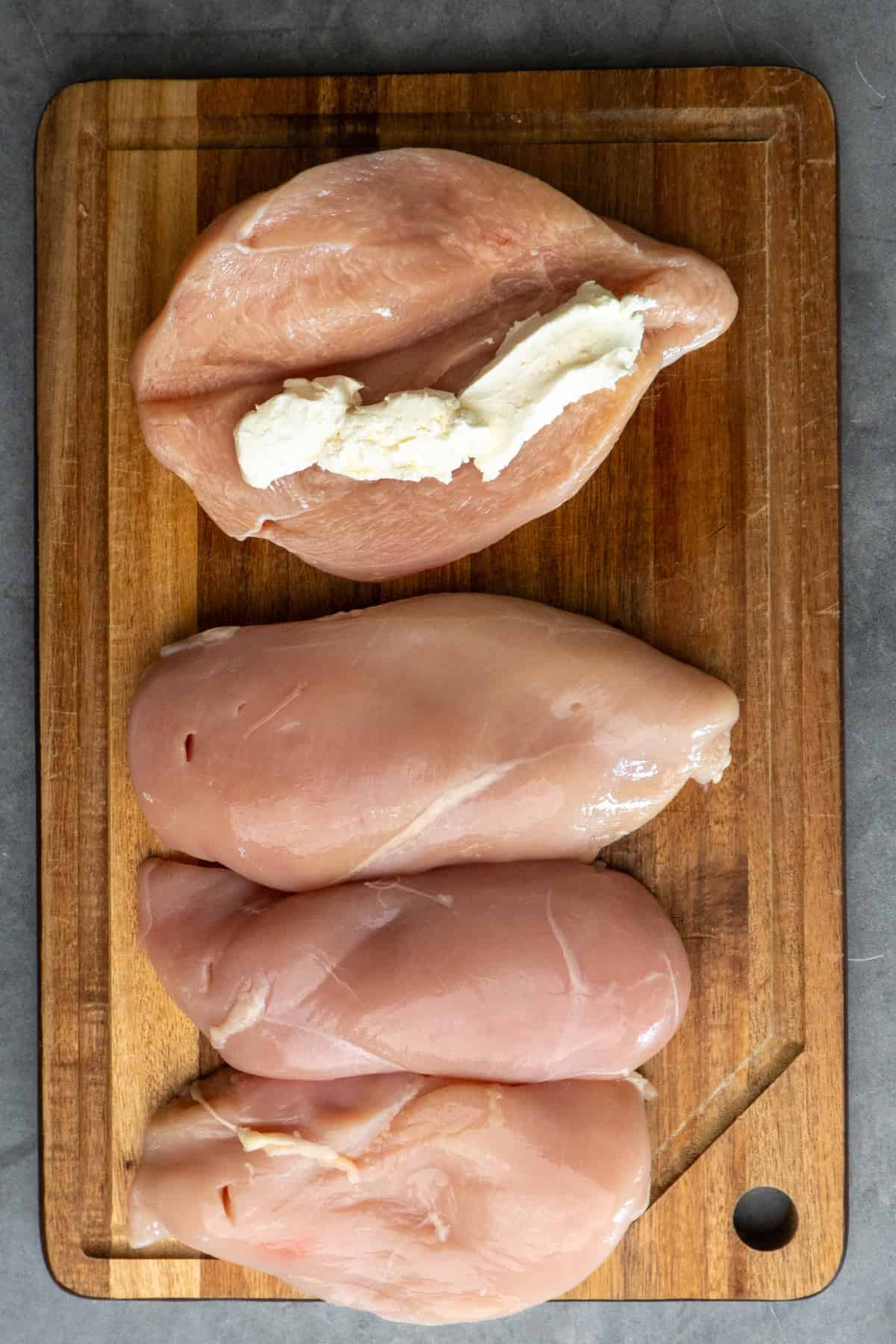 Chicken breasts on a wood cutting board cut open with cream cheese in the center.