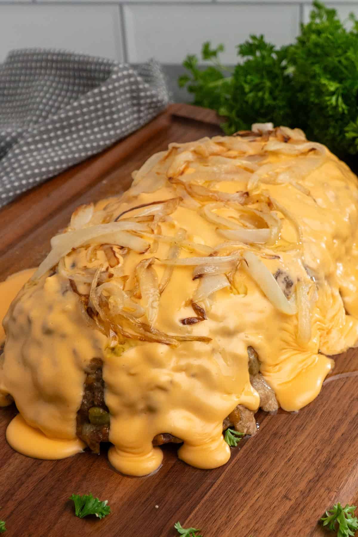 Cheese wiz and sautéed onions over a Philly cheesesteak meatloaf on a wood cutting board.