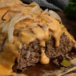 Philly cheesesteak meatloaf on a wood cutting board with a piece cut off.