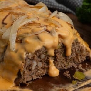 Philly cheesesteak meatloaf on a wood cutting board with a piece cut off.