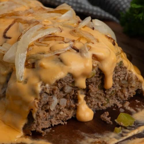Philly cheesesteak meatloaf on a wood cutting board with a piece cut off.