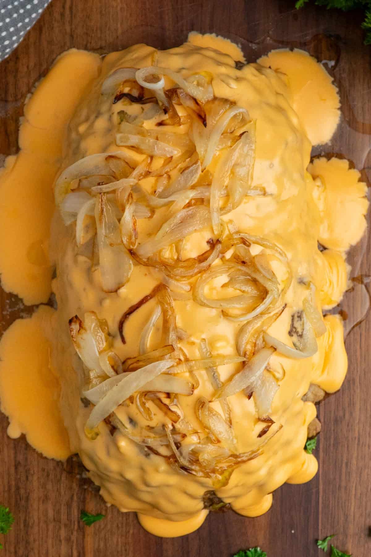 Cheese wiz and sautéed onions over a meatloaf on a wood cutting board.
