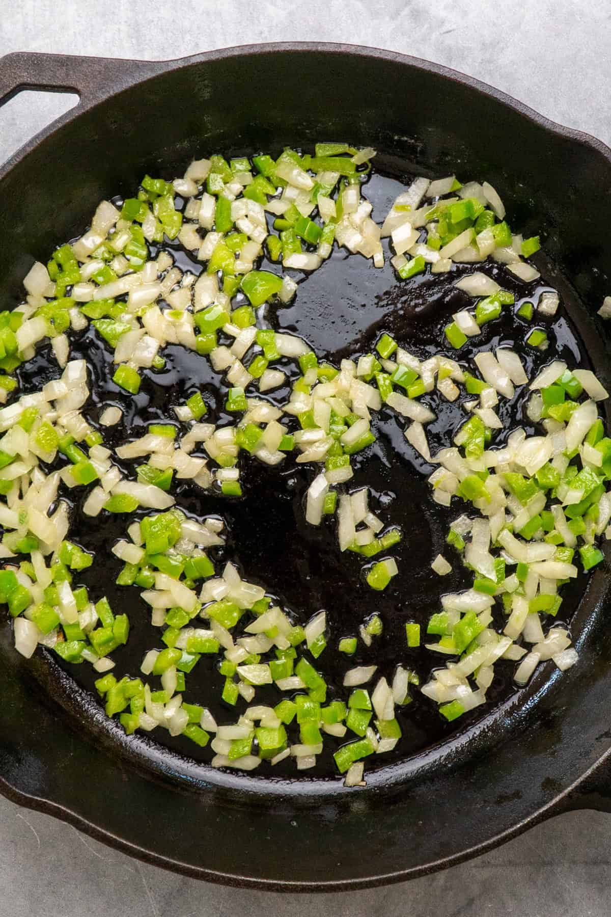 Onions and green bell peppers sauteing in a cast iron skillet.