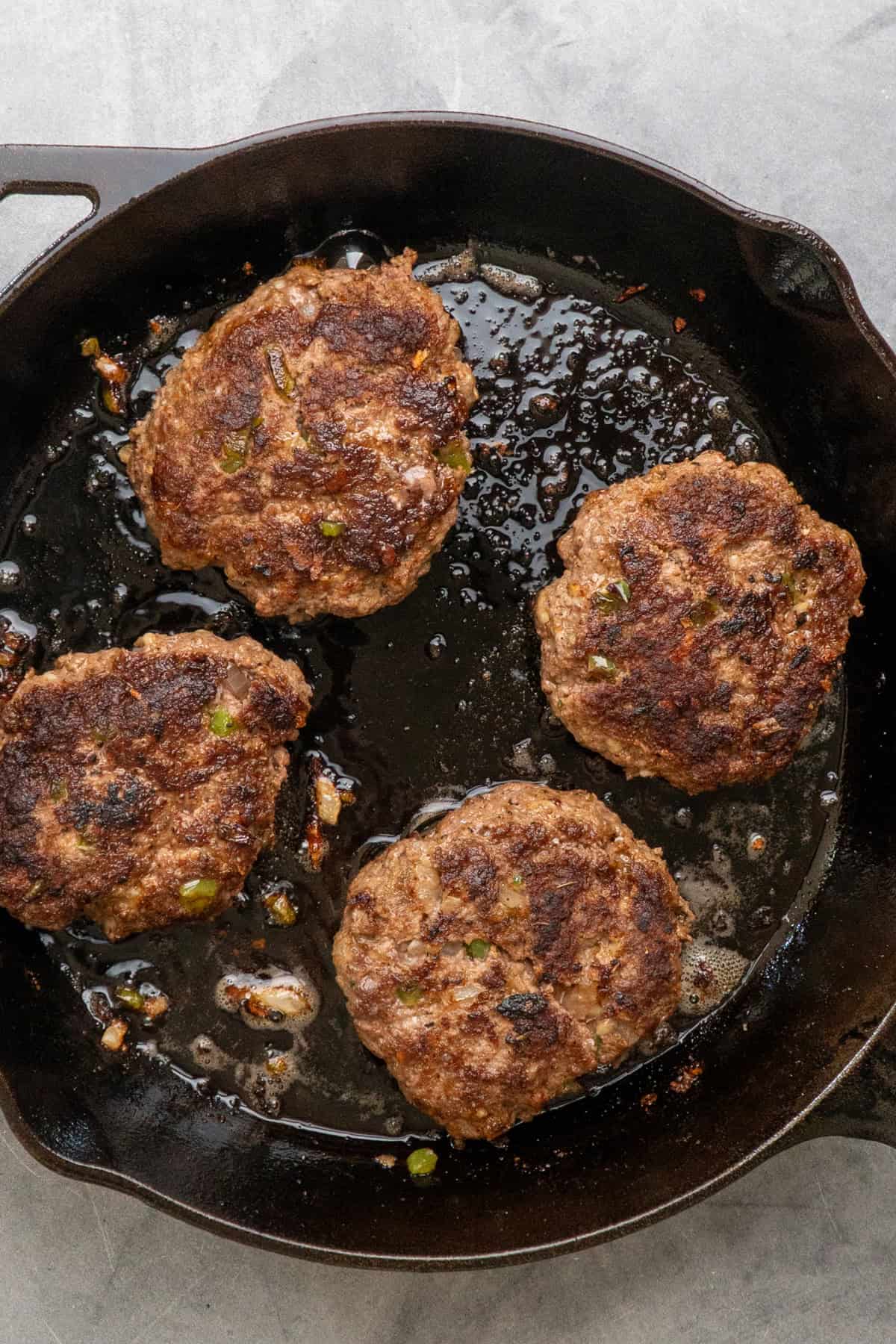 Four hamburger steak patties cooking in a cast iron skillet.