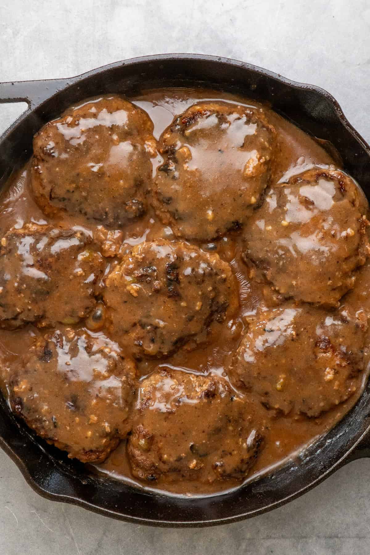 Hamburger steak patties simmering in gravy.