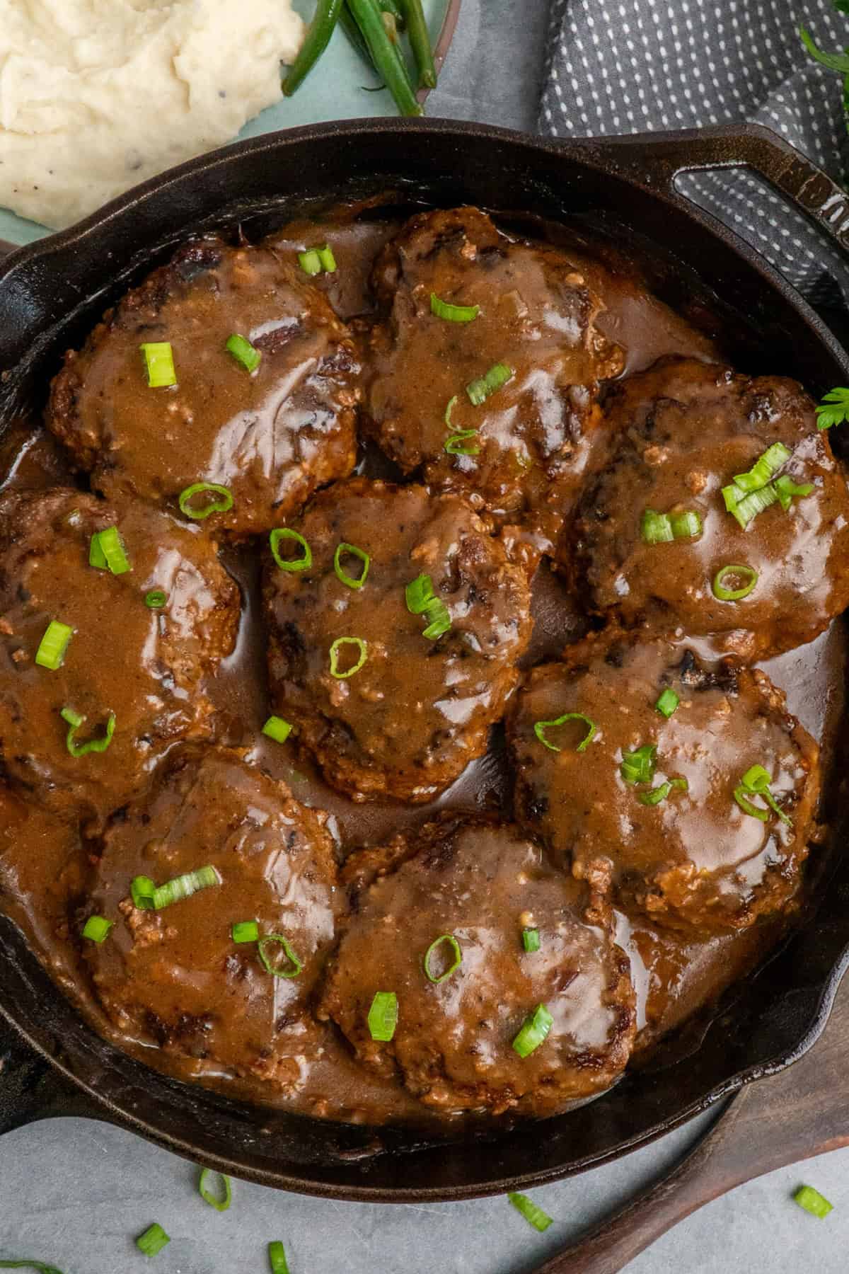 Salisbury steak recipe in a skillet and garnished with green onions.