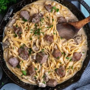 Fettuccine Alfredo with steak in a skillet and a wooden spoon to serve it.