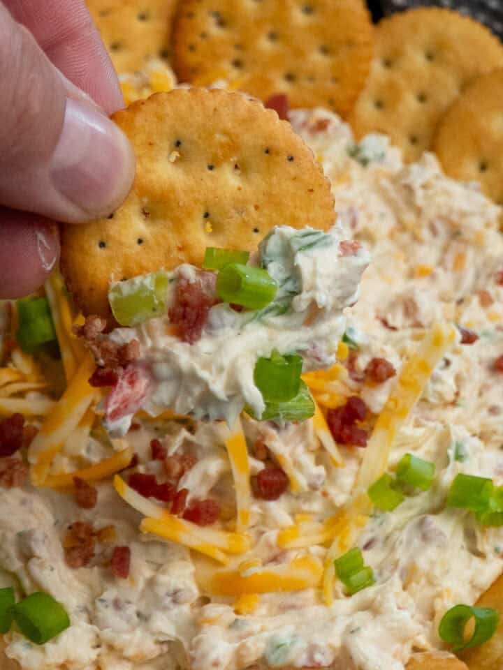 A hand holding a cracker covered in million dollar dip.