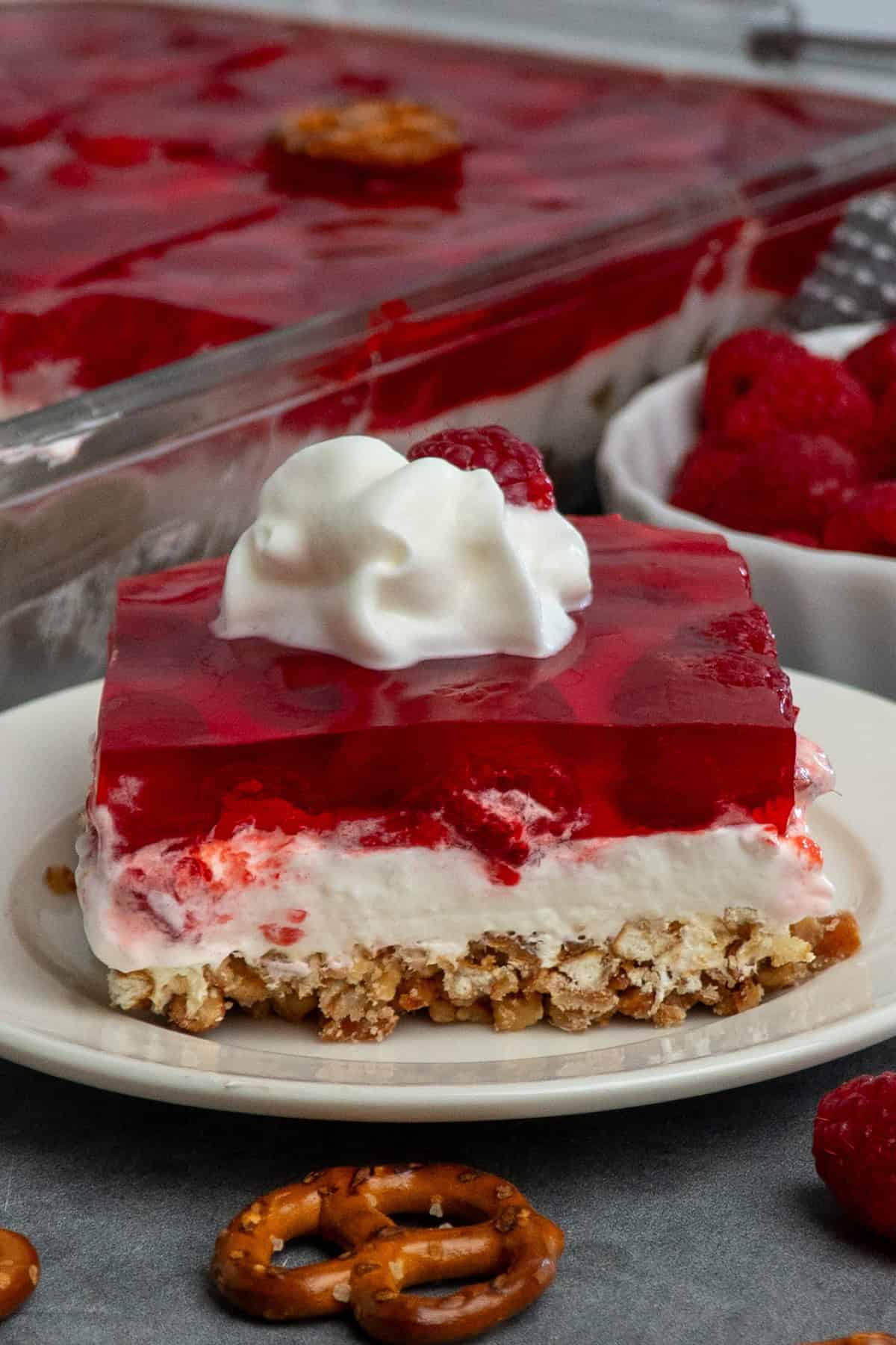 Raspberry pretzel salad on a plate and topped with whipped cream.