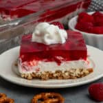 Raspberry pretzel salad on a plate and topped with whipped cream.